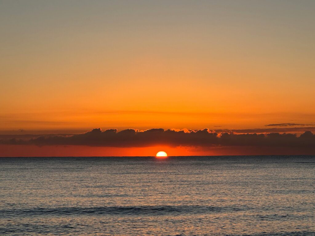 Serene ocean sunrise with vivid orange hues and gentle waves.